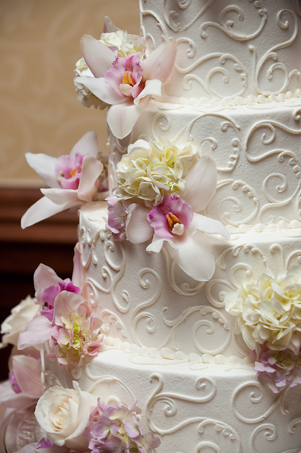Ivory four tiered wedding cake with whimsical design on borders and light pink, lavender, ivory, and light yellow floral accents - photo by Houston based wedding photographer Adam Nyholt